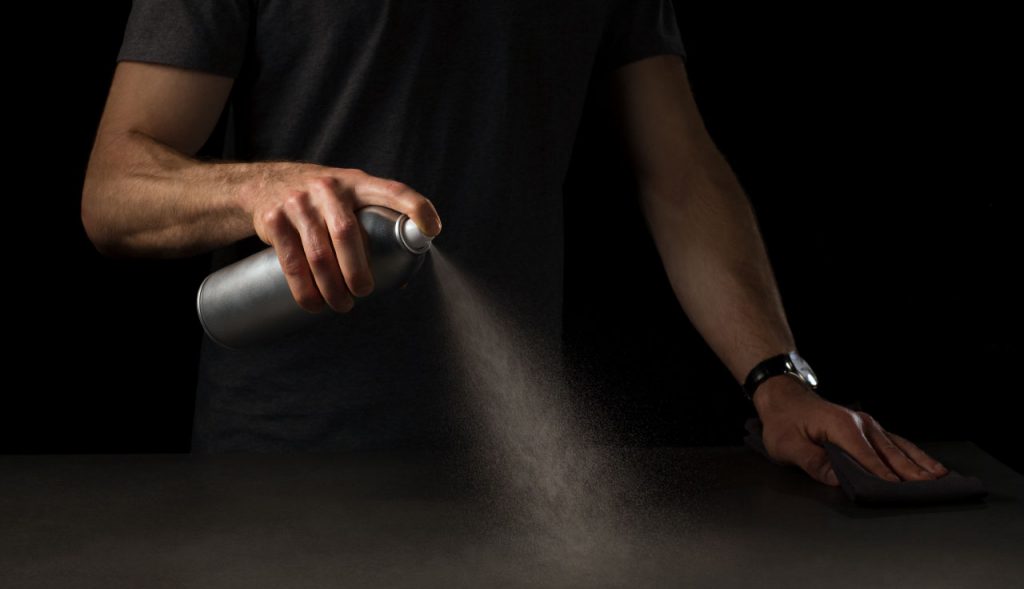 Man using a bag-on-valve spray system to apply a household cleaning product to a table.